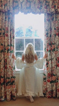 a girl in a white dress looking out of a window